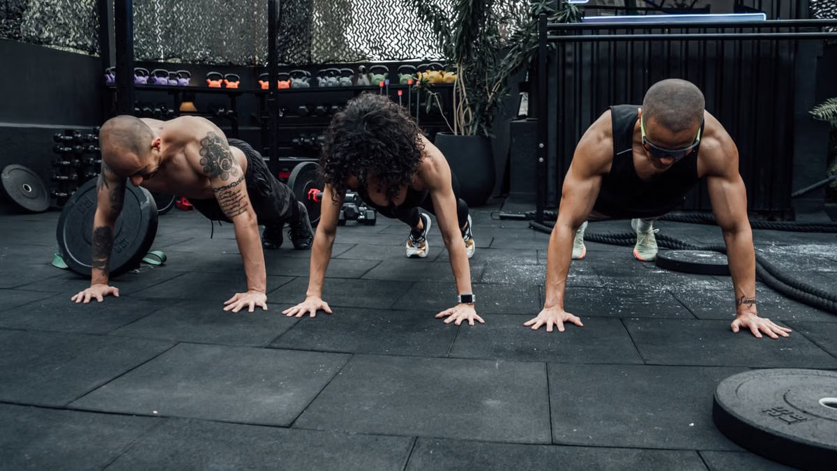 Three individuals performing push-ups together in a Mexico City gym setting.
